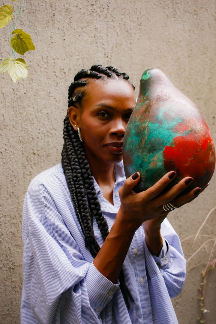 Mulher negra segurando uma cabaça artesanal pintada em verde e vermelho